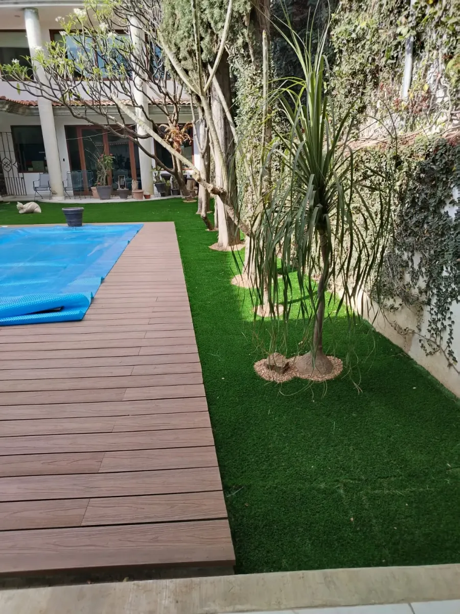 Alberca con terraza de madera y pasto sintético alrededor