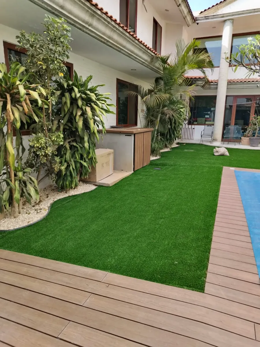 Jardín residencial con alberca, terraza de madera y pasto sintético
