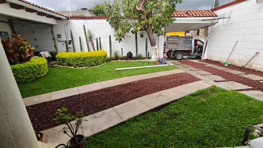 Jardín frontal con camino de losas, franja de grava roja decorativa y cactus