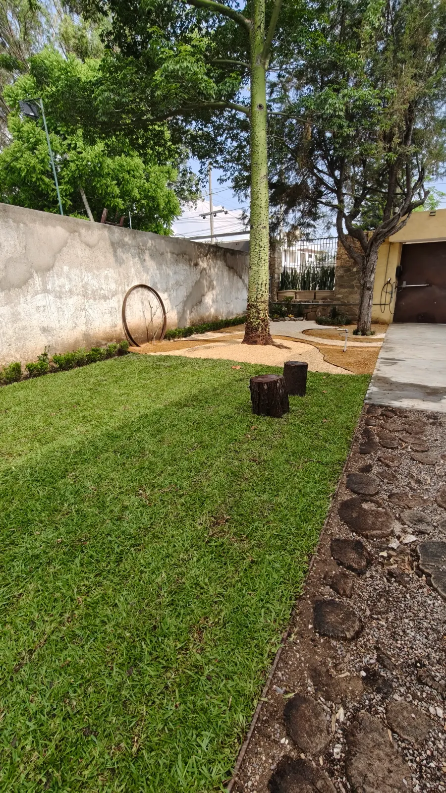 Jardín con diseño artístico, camino de rodajas de madera y escultura circular