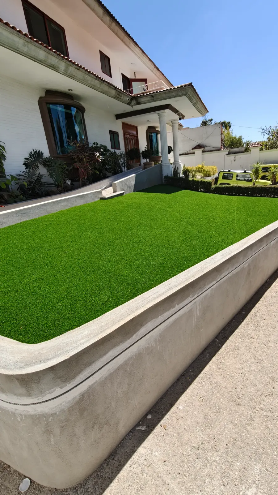 Jardín frontal de pasto sintético con muro curvo de concreto