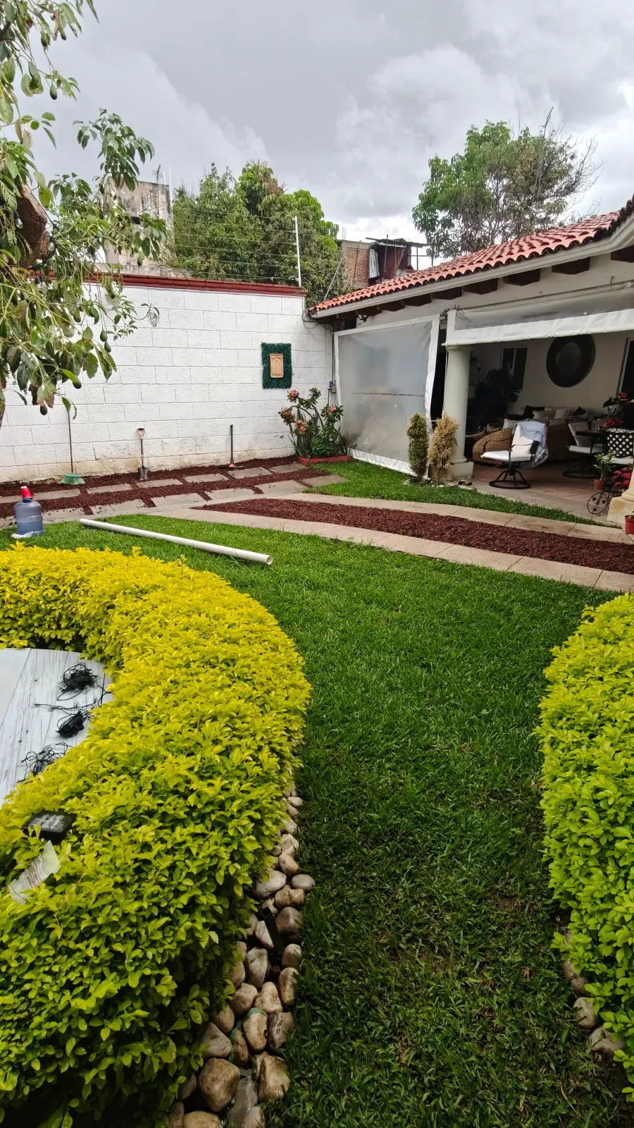 Patio con setos recortados, piedra bola decorativa y franja de grava roja